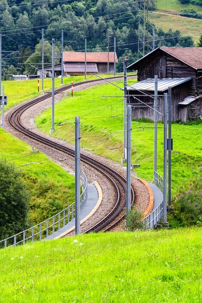 スイスアルプスの明るい緑の芝生を蛇行鉄道線路 — ストック写真