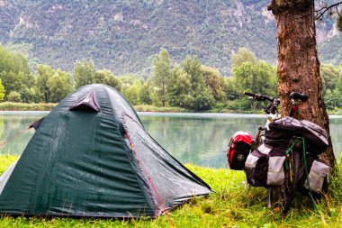 SION, SWitzERLAND - 12 Ağustos 2014 tarihinde Sion yakınlarındaki İsviçre Alplerinde yağmurlu bir sabahta gölün kenarında yalnız bir kamp alanı. Bisiklet ve kamp bir ülkeyi ziyaret etmenin popüler bir yoludur..