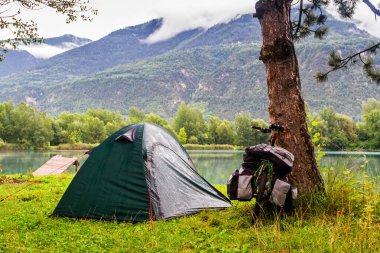 SION, SWitzERLAND - 12 Ağustos 2014 tarihinde Sion yakınlarındaki İsviçre Alplerinde yağmurlu bir sabahta gölün kenarında yalnız bir kamp alanı. Bisiklet ve kamp bir ülkeyi ziyaret etmenin popüler bir yoludur..