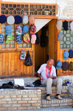 BÜKHARA, UZBEKISTAN - 15 Ağustos 2015: Buhara, Özbekistan, Orta Asya 'daki dükkanının önünde şapka tamir eden yaşlı adam