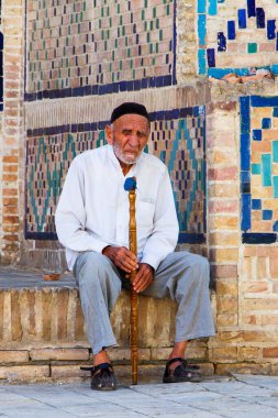 BÜKHARA, UZBEKISTAN - 9 AĞUSTOS: 9 Ağustos 2015 tarihinde Özbekistan 'ın Buhara kentindeki caminin önünde oturan adam. Buhara 'da geleneksel çiçek desenli bir duvar manzarası. Özbekistan, Orta Asya