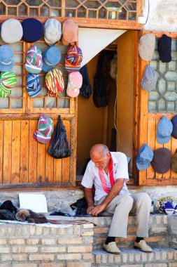 BÜKHARA, UZBEKISTAN - 15 Ağustos 2015: Buhara, Özbekistan, Orta Asya 'daki dükkanının önünde şapka tamir eden yaşlı adam