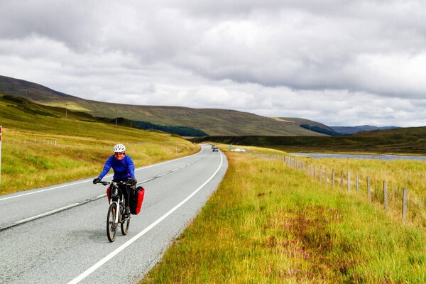 HIGHLANDS, SCOTLAND - AUGUST 15, 2016: Solo female cyclist cycle through Scottish mountains with her bicycle fully loaded with equipment and camping gear.