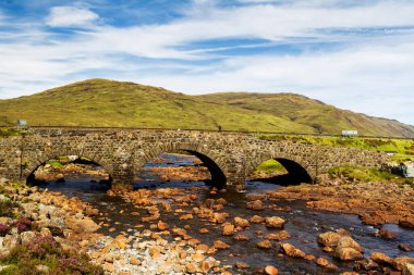 İskoçya 'nın Sligachan, Skye Adası' ndaki eski bir köprü İskoç manzarası, bitki örtüsü, tepeler ve taze mavi suyu ve güneşli gökyüzü ile birlikte. Birleşik Krallık, İngiltere