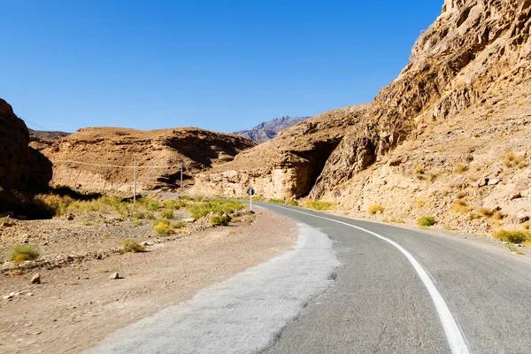 Beautiful scenic view - twisty road across the dry arid land between barren mountains against the background of vivid blue sky. Road to Abyaneh, Iran