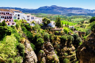 Güneşli bir günde İspanya 'nın güneyindeki Andalucian kasabasında kayalıklardan sarkan evler. Ronda, beyaz şehir rotasında popüler bir turizm merkezidir ve çoğu turist tarafından sık sık ziyaret edilir.