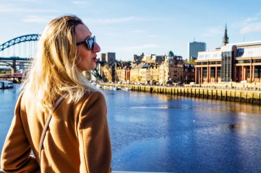 NEWCASTLE UPON TYNE, İngiltere - 28 Ekim 2017: Güzel sarışın kız ayakta duruyor ve Tyne Nehri 'ne bakıyor İngiltere, Tyne üzerinde köprüler ile