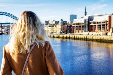 NEWCASTLE UPON TYNE, İngiltere - 28 Ekim 2017: Sarışın kız Tyne Nehri 'nde dikilen ve Newcastle' da köprüler olan Tyne Nehri 'ne bakıyor