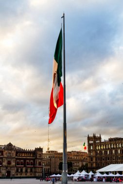 Büyük bir Meksika bayrağı (İspanyolca: Bandera de Mexico), Meksika 'nın Zocalo şehrinde, mavi gökyüzü olan bayrak direğinde, gün batımından önce altın ışıkla aydınlatılır.