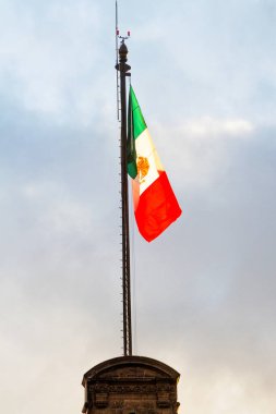 Büyük bir Meksika bayrağı (İspanyolca: Bandera de Mexico), Meksika 'nın Zocalo şehrinde, mavi gökyüzü olan bayrak direğinde, gün batımından önce altın ışıkla aydınlatılır.