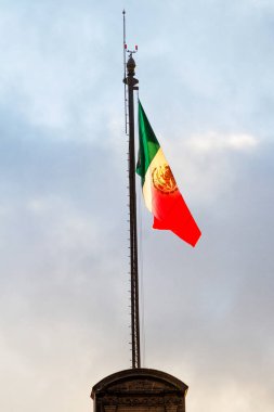Büyük bir Meksika bayrağı (İspanyolca: Bandera de Mexico), Meksika 'nın Zocalo şehrinde, mavi gökyüzü olan bayrak direğinde, gün batımından önce altın ışıkla aydınlatılır.