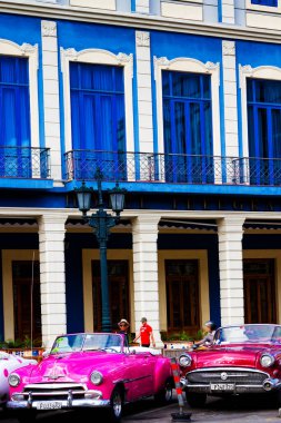 HAVANA, CUBA - 14 Kasım 2017: İnsanlar, eski arabalar ve renkli binaların olduğu tipik sokak sahnesi. 2 milyondan fazla nüfusuyla Havana, Küba 'nın başkenti ve Karayipler' in en büyük şehridir.