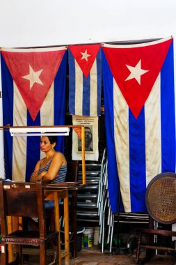 HAVANA, CUBA - No 27, 2017: Ulusal bir fabrikada Küba bayraklarının altında masa başında oturan kadın.