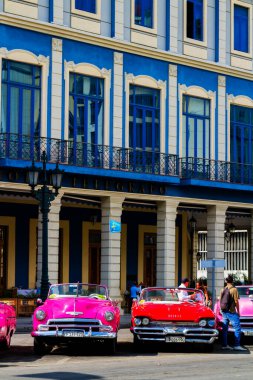 HAVANA, CUBA - 14 Kasım 2017: İnsanlar, eski arabalar ve renkli binaların olduğu tipik sokak sahnesi. 2 milyondan fazla nüfusuyla Havana, Küba 'nın başkenti ve Karayipler' in en büyük şehridir.