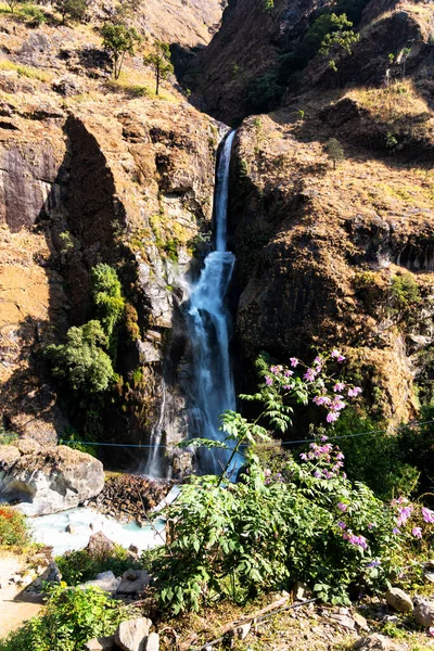 A waterfall spotted in Tal, Annapurna Circuit Trek, Nepal. Few hundred meters of free fall, waterfall surrounded by tall mountains slopes, covered with green bushes and trees.