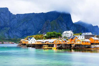 Norveç 'in Lofoten Adaları' ndaki kırmızı ve sarı rorbu evleriyle ünlü bir turistik bölge olan Hamnoy balıkçı köyü. Sakin, bulanık su