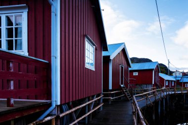 Nusfjord limanında renkli kırmızı balıkçı evleri ve Norveç 'in Lofoten Adaları' nda huzurlu bir akşamda yelkenli tekneleri var.