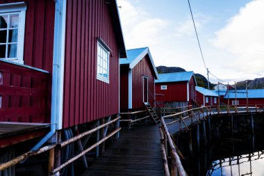 Nusfjord limanında renkli kırmızı balıkçı evleri ve Norveç 'in Lofoten Adaları' nda huzurlu bir akşamda yelkenli tekneleri var.