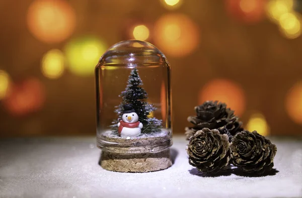 クリスマス明るい背景から分離された円錐形の松の近くのガラス管にクリスマス ツリーと雪の男 — ストック写真