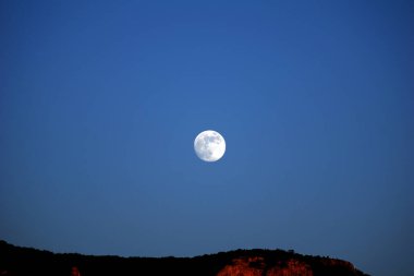 Gün batımında dağların üzerinde dolunay doğuyor.
