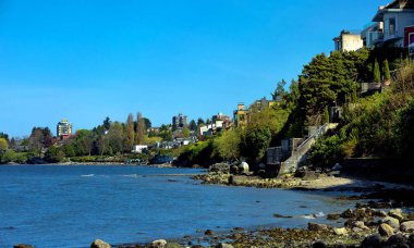 Vancouver, Kitsilano bölge. Düşük tide saat denizde taşlı eğimi City'de eteklerinde. Denize bakan bir yerleşim bölgesinde backyards arka plan mavi bir gökyüzü desteklemek.. 