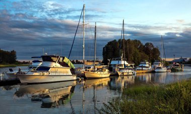 Motorlu tekneler ve yatlar köy yakınlarındaki marinada balıkçı teknelerinin akşam saatlerinde, dağ sırası ve bulutlu gökyüzü arka planda