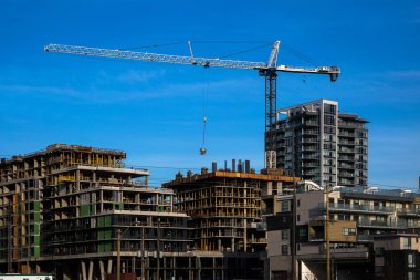 Burnaby şehrinde yüksek katlı binaların yeni inşaatı, endüstriyel şantiye, inşaat ekipmanları, bitmiş gökdelenler ve açık bulutlar ile mavi gökyüzü arka plan üzerinde çeşitli inşaat vinçler