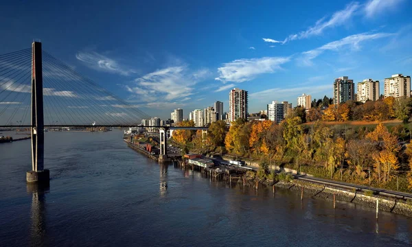 New Westminster City the slopes of the Fraser River, painted with autumn colors, Sky Train Bridge and a  road against the background of a bright sky with white clouds