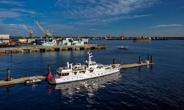 Vancouver Harbor ticari kargo limanı ve marina zevk yatlar için, savaş gemisi iskelede demirlemiş, kalkışta hidrouçak, mavi bulutlu gökyüzünün arka planında ufukta Vancouver City