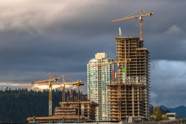 Coquitlam City 'de yeni yüksek binalar, endüstriyel inşaat alanı, inşaat ekipmanları, fırtınalı bulutlu gökyüzünün arka planında birkaç inşaat vinci.