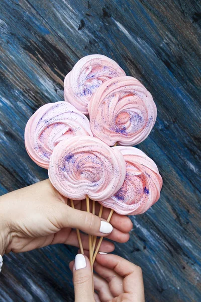 Pink meringues with sparkles on sticks in hands on vintage backg