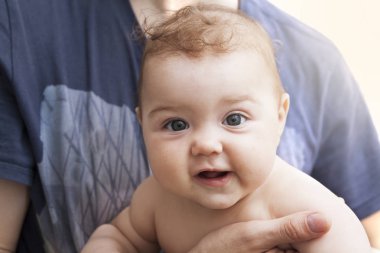 Çocuk babasının ellerinde gülümsüyor.