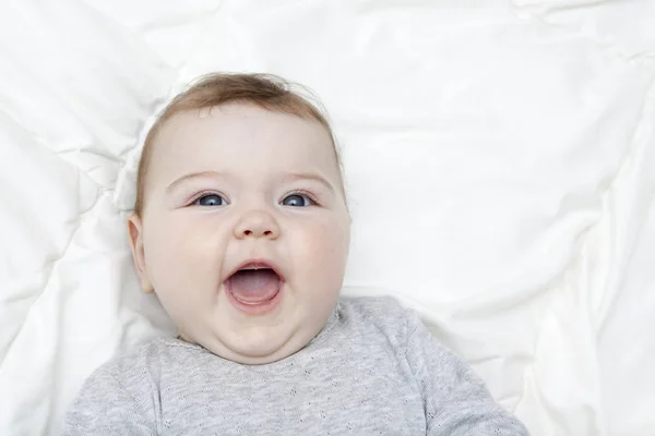 Anak itu tertawa dengan mulut terbuka tergeletak di tempat tidur putih — Stok Foto