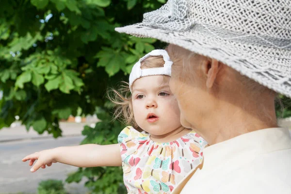 A menina nos braços de sua avó em uma caminhada de verão na rua. Velhos e pequenos, duas gerações — Fotografia de Stock