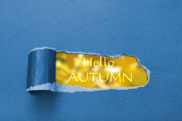 Text hallo Herbst und verschwommenes herbstgelbes Laub in einem zerrissenen Papierloch — Stockfoto