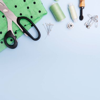 Mavi arka planda kumaş, iplik ve dikiş malzemelerinin üst görüntüsü. Kıyafet dikme konsepti. Boşluğu kopyala