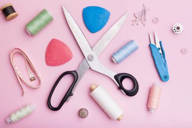 Makas, iplik ve dikiş malzemelerinin üst görüntüsü pembe arka planda. Kıyafet dikme konsepti.