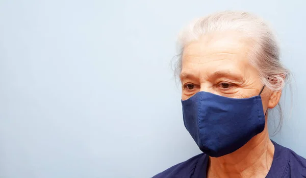 Senior woman in a cloth mask is not looking at the camera on a blue background. banner