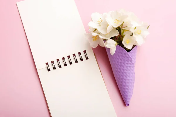 Blank notepad and flowers in a waffle cone on a pink background. Blank for congratulations, notes