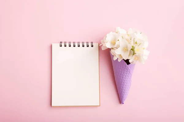 Blank notepad and flowers in a waffle cone on a pink background. Blank for congratulations, notes