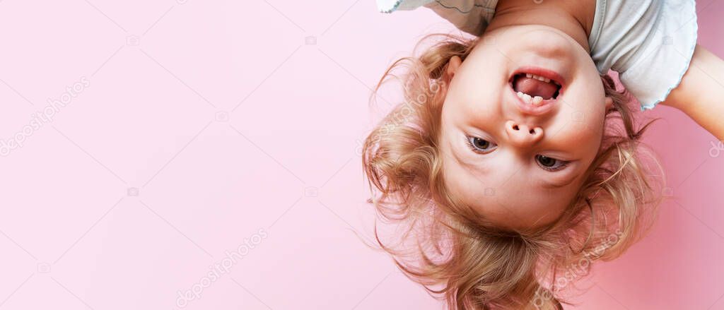 cute funny baby upside down looking at camera on pink background with copy space