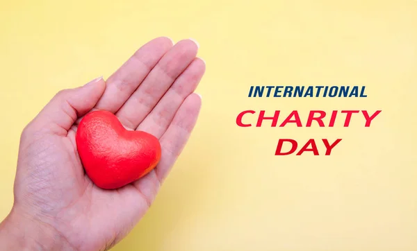 Coração vermelho na mão em um fundo amarelo com texto Dia Internacional da Caridade — Fotografia de Stock