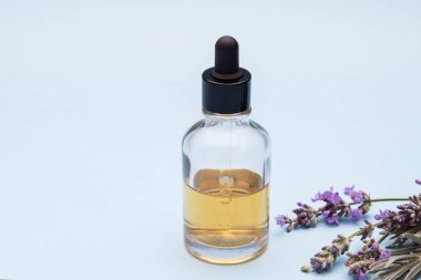 Mavi bir zemin üzerinde lavanta çiçekleri olan sıvı dolu cam bir şişe..