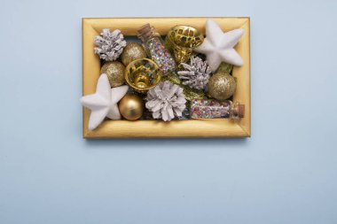 Beyaz yıkanmış çam kozalakları, çanlar ve diğer yeni yıl dekorları mavi arka planda altın bir fotoğraf çerçevesinde yatıyordu.