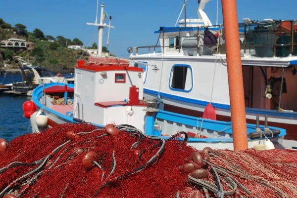 Fishing nets and fishing boats on the quay: A Mediterranean glimpse showing a pile of red fishing nets and some fishing boats on the quay.