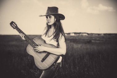 Genç kadın kırsal çayır arka gitar çalmaya şapkalı