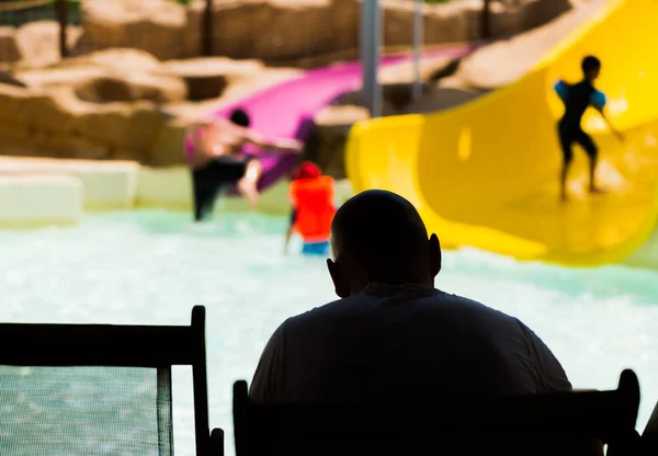 silhouette of bold man watching at kids playing in pool playground