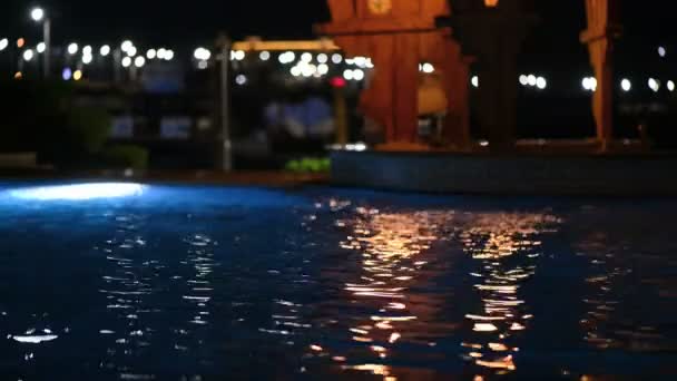 水平線の向こうの夜の通りの背景にプールの水に点滅する光と海辺の静かな風景 — ストック動画