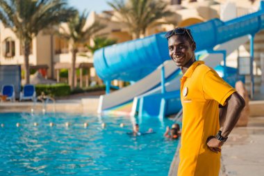 Mısır, Hurghada - 15.07.2020, arka planda yüzme havuzu alanında çalışan Mısırlı otel personelinin gülümseyen portresi.