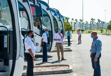 Mısır, Hurghada - 11.07.2020. Koruyucu maskeli tur rehberleri havaalanı yakınlarındaki otobüs durağında turistleri bekliyor. 